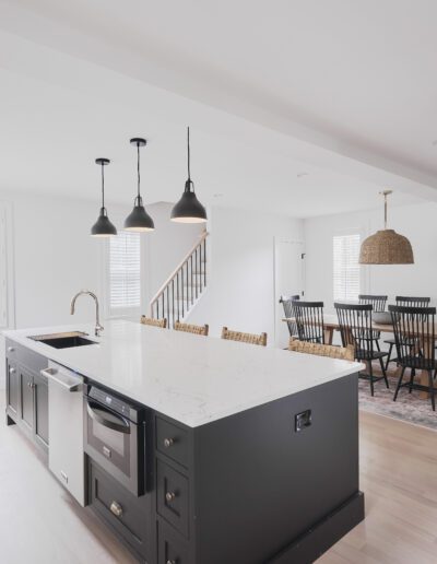 A modern kitchen with a large white island countertop, black base cabinets, pendant lights, and adjacent dining area with a wooden table and black chairs.