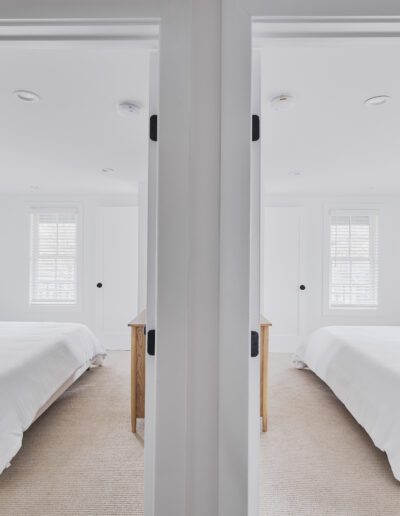 Two adjacent doorways open to identical bedrooms with white bedding, beige carpets, and windows with white blinds, separated by a central wall.