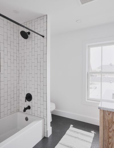 A modern bathroom with a white tiled shower, black fixtures, a white curtain, wooden vanity with marble countertop, rectangular mirror, white walls, and black hexagon floor tiles.