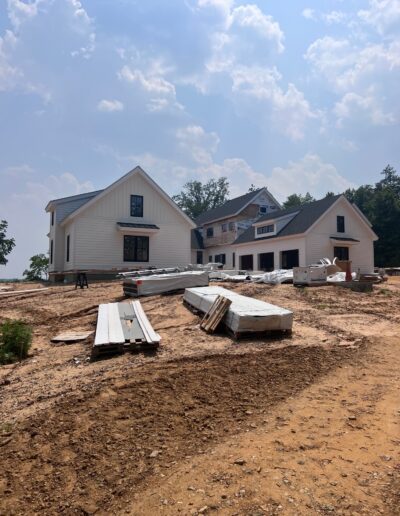 A construction site with two partially built houses, surrounded by stacks of building materials, under a partly cloudy sky.