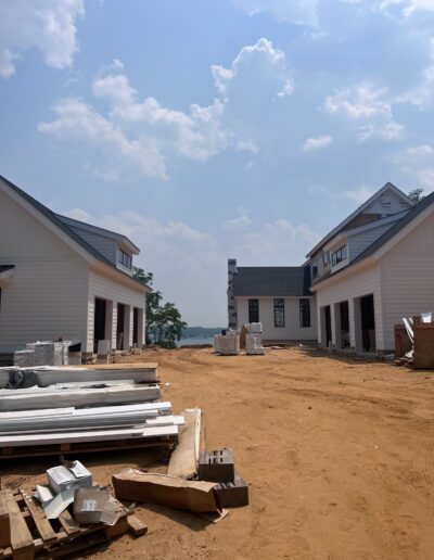 Construction site of new homes with building materials and tools scattered on a dirt path between two unfinished houses, under a partially cloudy sky.