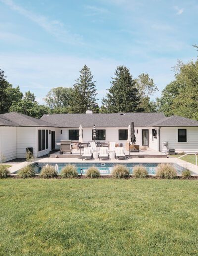 A modern single-story house with a large backyard featuring a swimming pool, outdoor seating area, and well-maintained lawn. Trees surround the property, creating a private and serene atmosphere.