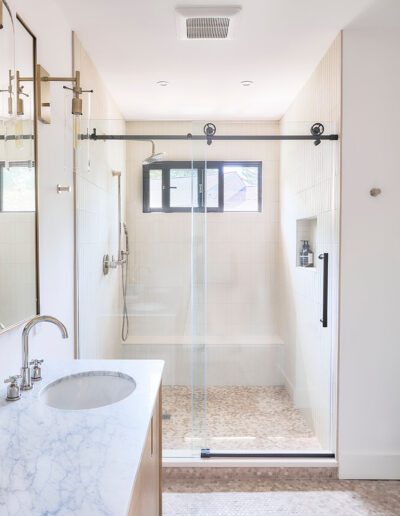 A modern bathroom with a marble countertop, a sink, a mirror, a towel, soap dispenser, and a glass-enclosed walk-in shower with a sliding door and overhead light.