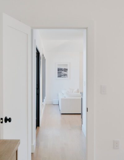 A view through open doors leading to a living area with a white couch and wall art, and a partial view of a bathroom on the right.