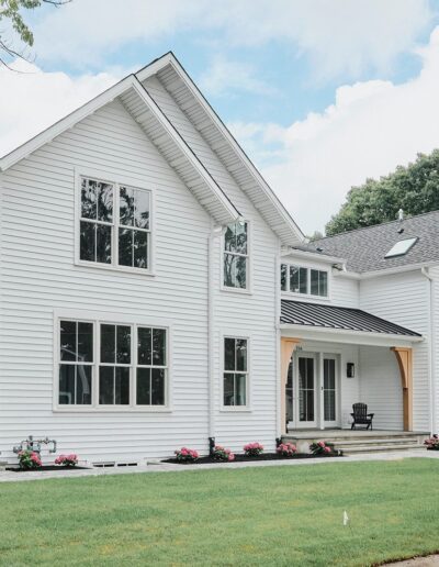 Modern two-story white house with large windows, a porch, and a well-maintained lawn. Trees and a cloudy sky in the background.