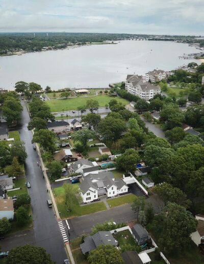 Aerial view of a residential neighborhood with houses, greenery, and a nearby large body of water on a cloudy day.