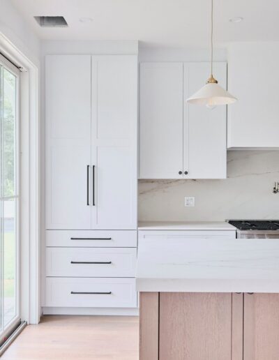 Modern kitchen with white cabinets, a wooden island, and a hanging pendant light. Large window to the left allows natural light to enter.