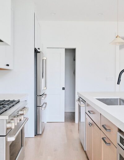 Modern kitchen with white cabinetry, stainless steel appliances, black faucet, and light wood flooring. Features a gas stove, sink island with storage, and pendant lighting.