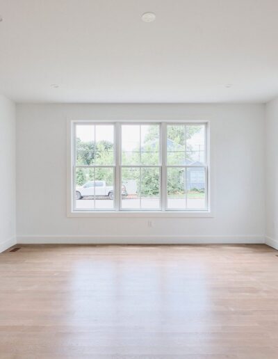 A spacious, empty room with light wooden flooring, large windows letting in natural light, and a built-in wall fireplace on the right side.