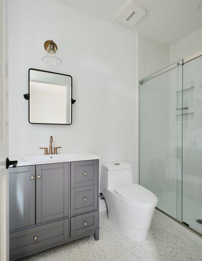 A modern bathroom featuring a gray vanity with a square mirror, a white toilet, and a glass-enclosed shower.