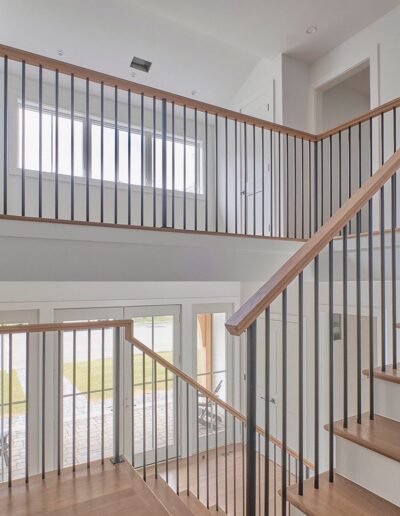 Modern staircase with wooden steps and metal railings leading to an upper floor in a well-lit interior space with large windows.